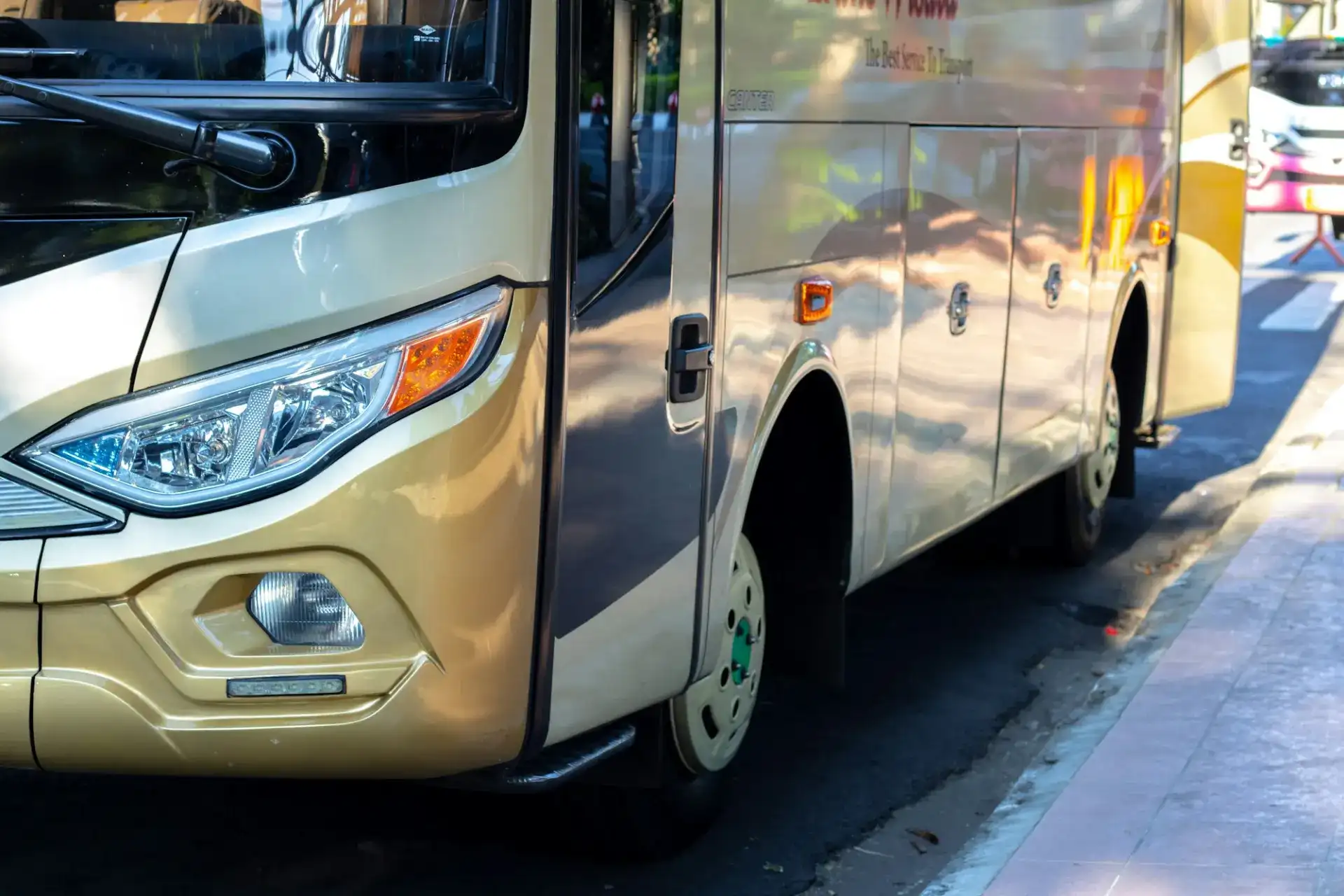 A tan coach bus parked at a curb seen from the front corner