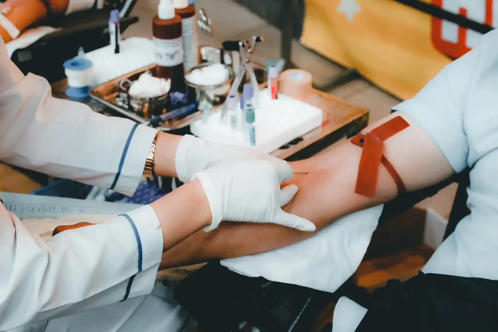 Gloved hands drawing blood from a patient's arm with a tourniquet and specimen tubes on the tray