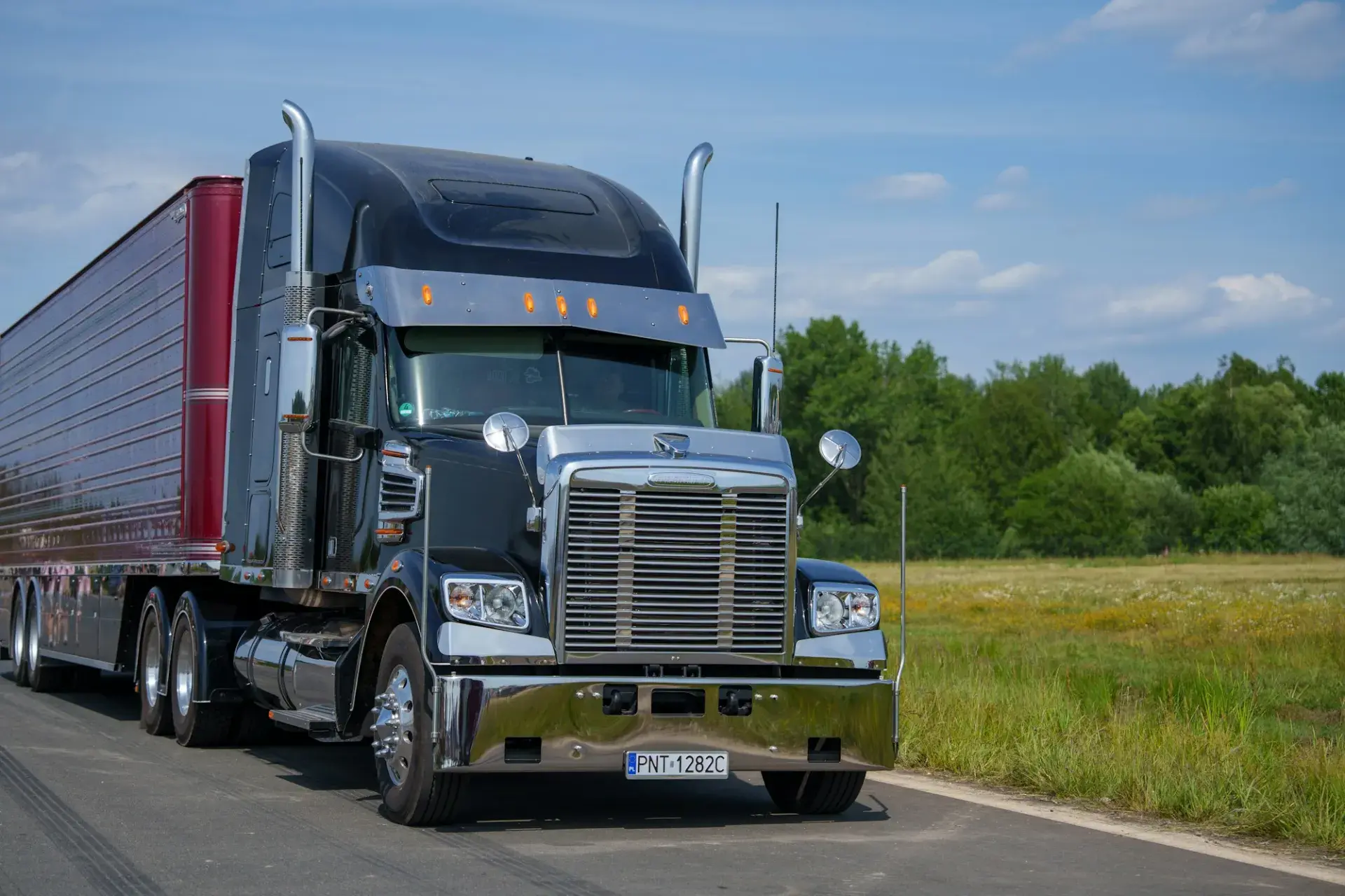 A black tractor-trailer with chrome stacks parked on a road beside a field