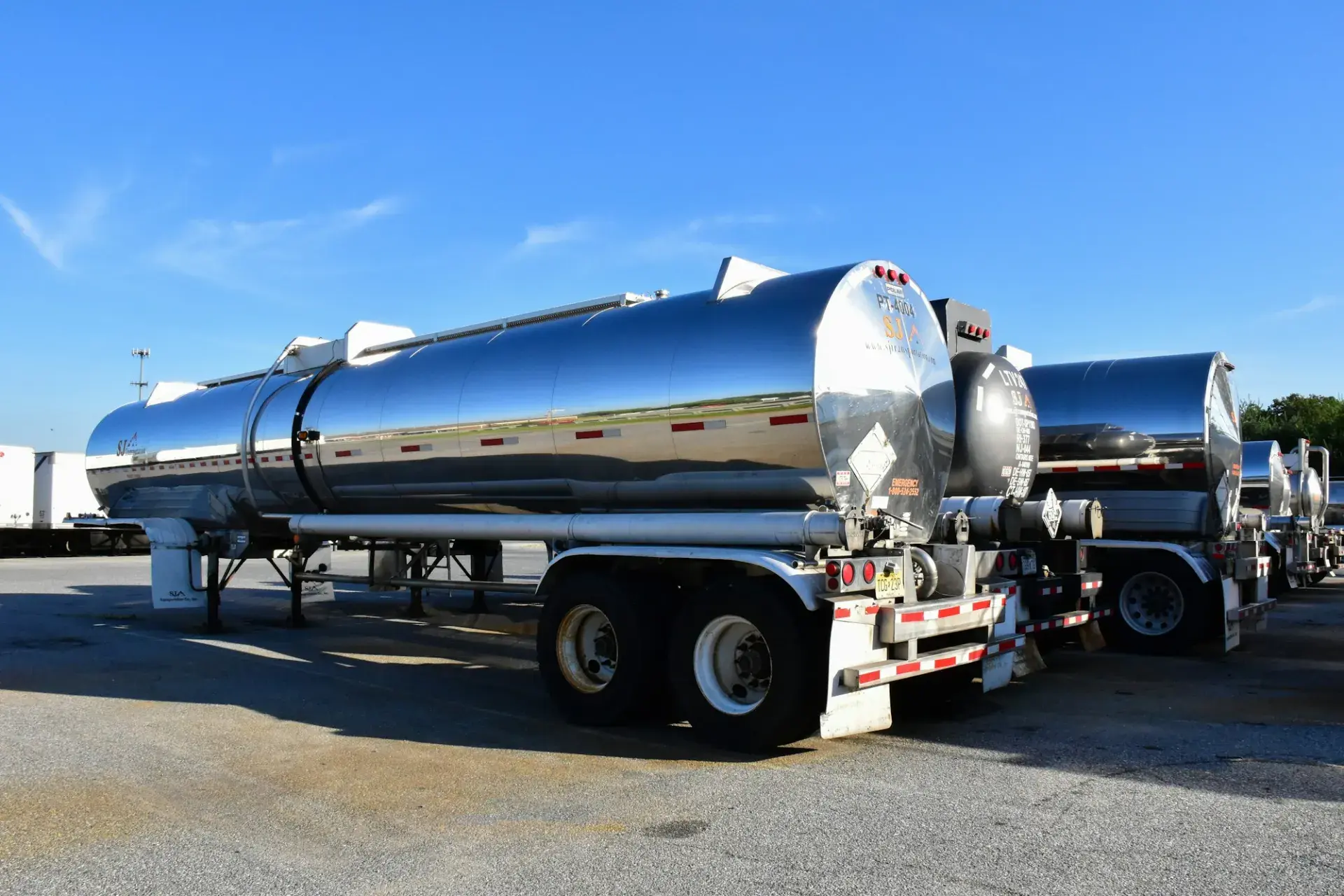 Polished stainless steel tank trailers parked in a lot under a blue sky
