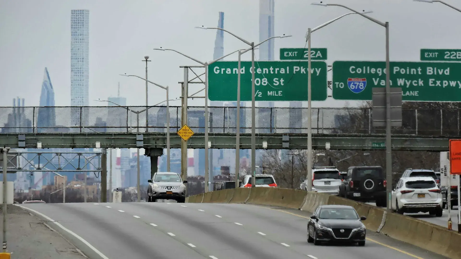 Traffic on a Queens highway with overhead exit signs and the Manhattan skyline behind