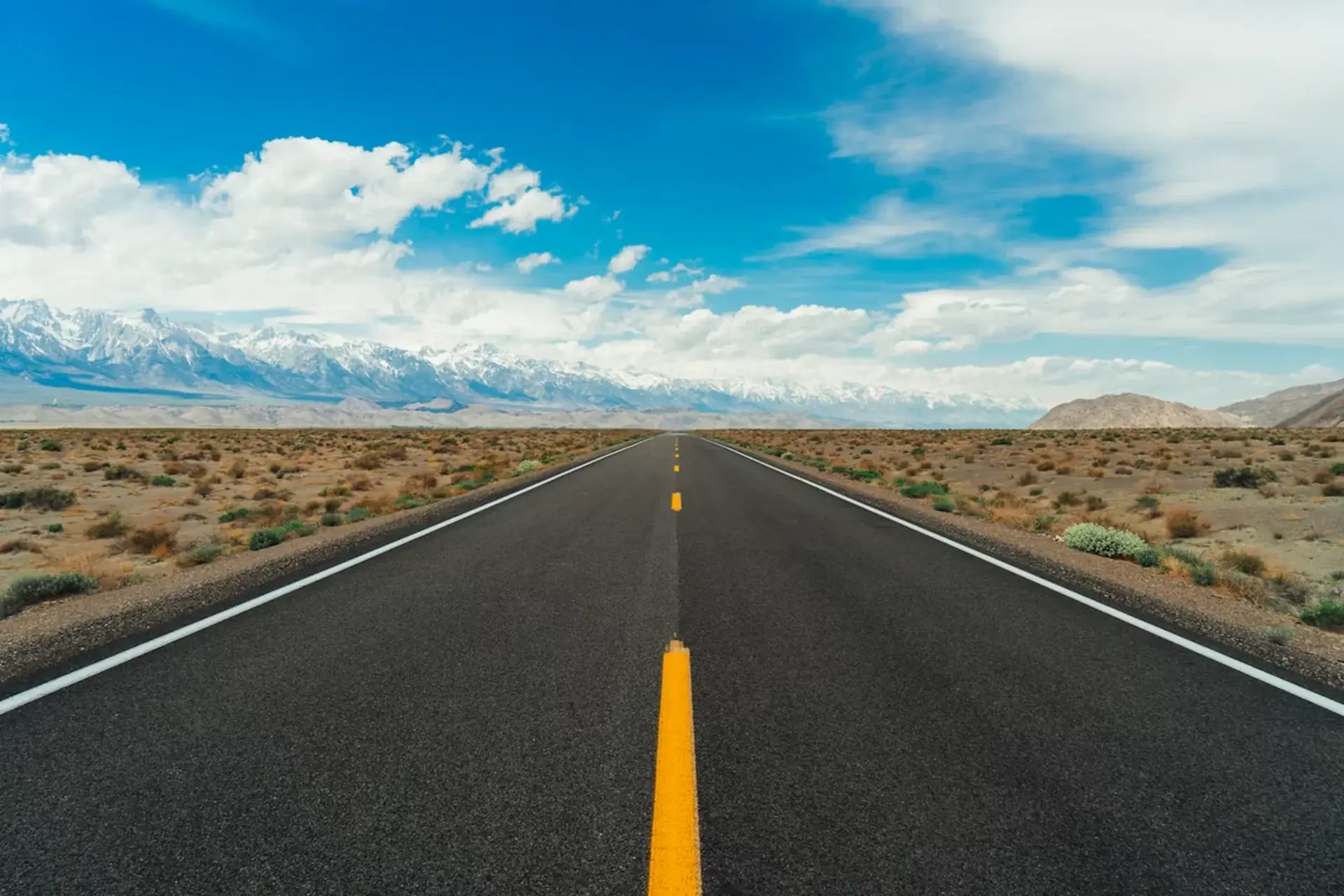 Grey asphalt highway leading toward rugged mountains under open sky in Utah