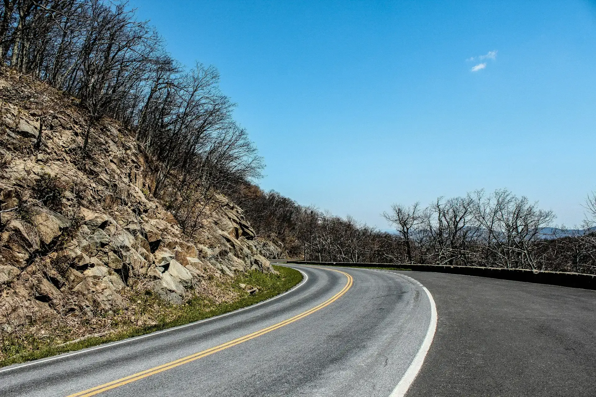 Skyline Drive curving past a rock cut under a blue sky in Shenandoah National Park, Virginia