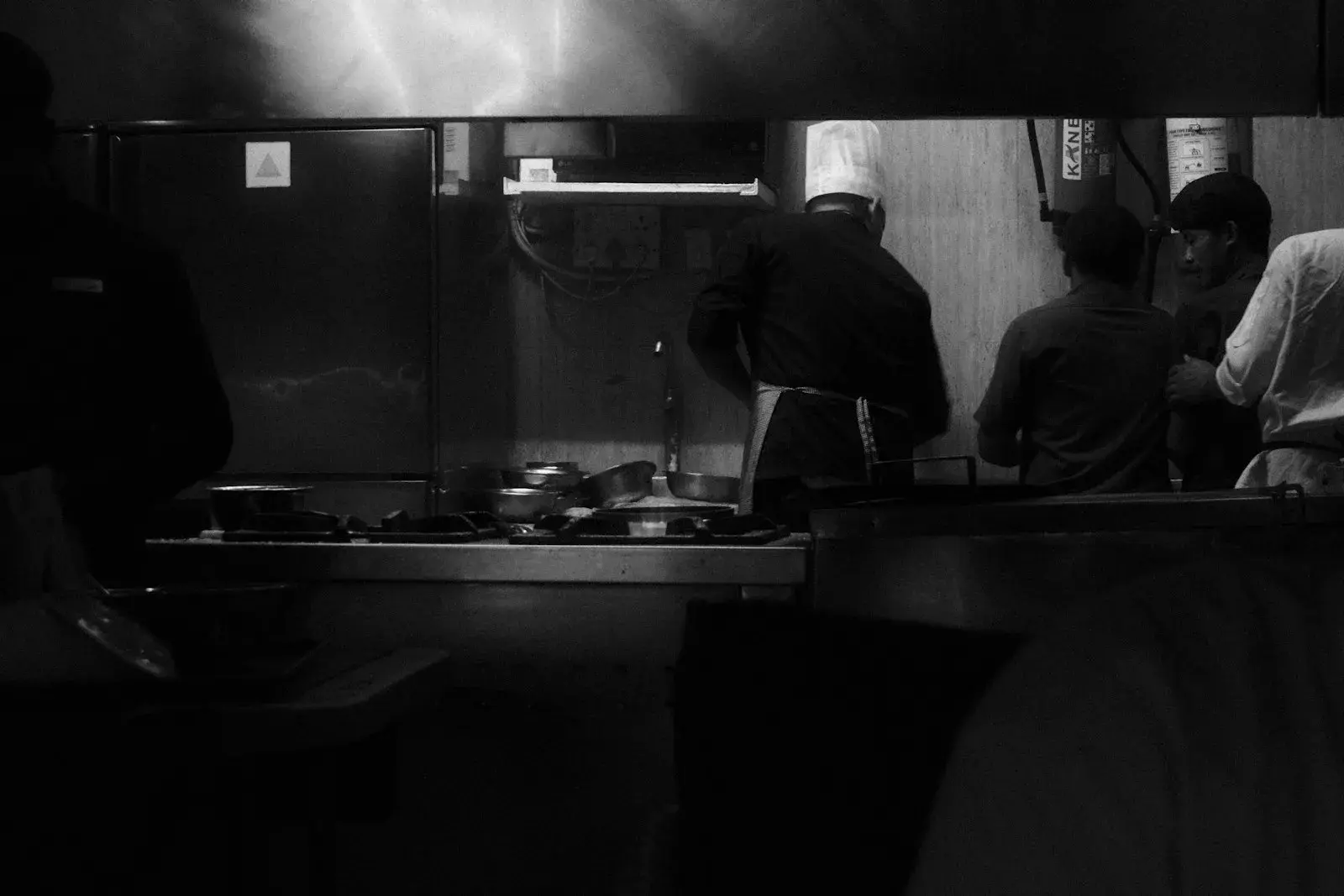 Chefs preparing food in a busy commercial restaurant kitchen with stainless steel counters and heat lamps