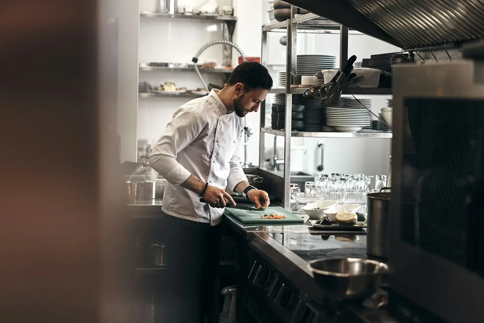 Chef in whites preparing food at the counter of a stainless steel restaurant kitchen